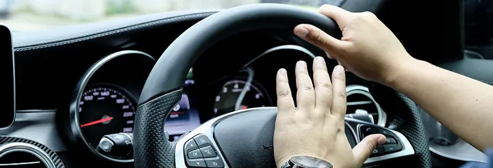 A hand pressing the horn in the centre of a steering wheel