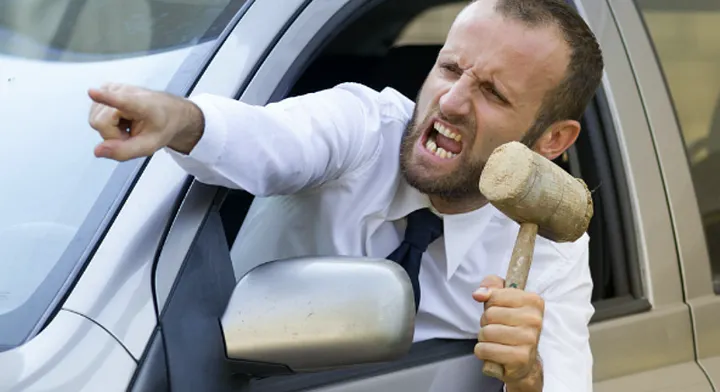 An angry driver leaning out of the window, shouting and brandishing a mallet
